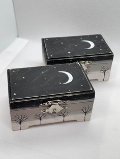 two black and silver boxes sitting on top of a white surface with trees in the background