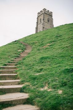 a stone tower on top of a grassy hill with steps leading up to the top