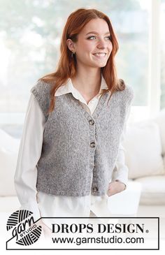 a woman standing in front of a white couch wearing a gray sweater vest and white pants