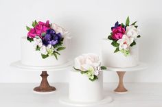 three tiered cakes with flowers on them sitting on top of each other in front of a white wall