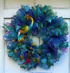 a blue and green wreath with peacocks on it's side hanging from a white door