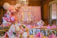 a room filled with lots of tables covered in pink and white balloons next to a chandelier