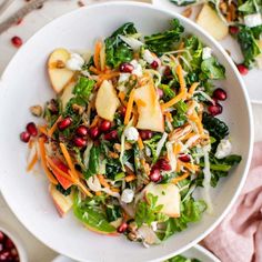 a salad with apples, carrots and cheese in a white bowl on a table