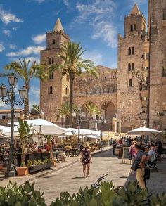 people are walking around an outdoor market in front of a large building with tall towers