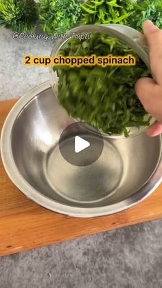 a person is holding some greens in a metal bowl on a wooden board with the words, 2 cup chopped spinach