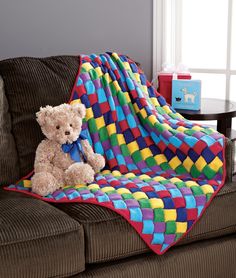 a teddy bear sitting on top of a couch next to a colorful blanket that is covering it