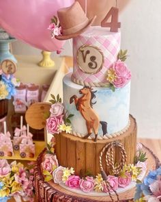 a three tiered birthday cake decorated with pink and blue flowers, balloons and horses