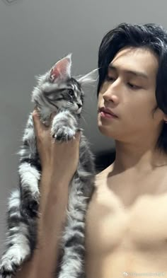 a shirtless man holding a cat in his right hand and looking at the camera