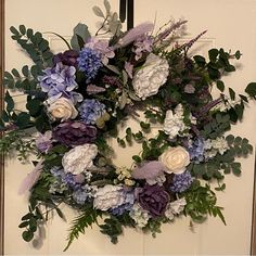 a wreath with purple and white flowers hanging on a door