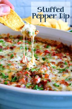 a hand holding a tortilla chip and dipping it into a casserole dish