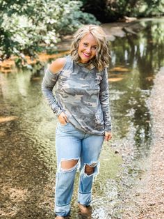 a woman is standing in the water wearing ripped jeans and a camo top with cutouts