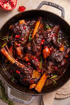 a pan filled with meat and vegetables on top of a table next to pomegranates