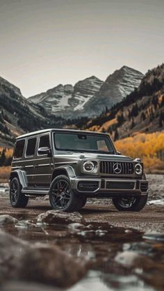 the mercedes g class is parked in front of mountains