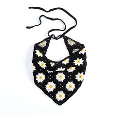 a black and white crocheted bib with daisies on it, hanging from a string