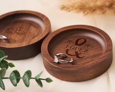 two wedding rings are placed in a wooden ring dish on a white tablecloth with greenery