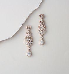 two pairs of diamond earrings sitting on top of a white surface