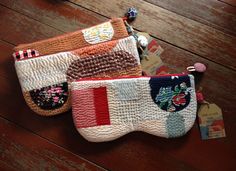 three small purses on a wooden floor with tags attached to the handles and sides