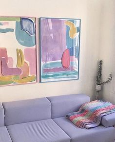 two paintings hang on the wall next to a blue couch in a room with white walls