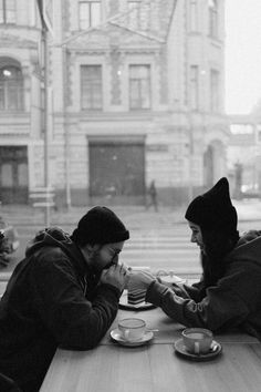 two people sitting at a table with plates of food and cups in front of them