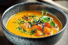 a bowl of soup with carrots and spinach garnish