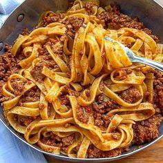 a pan filled with pasta and meat sauce on top of a wooden table next to a fork