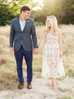 a man and woman holding hands while walking through the grass