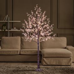 a lighted tree in the middle of a living room next to a couch and coffee table