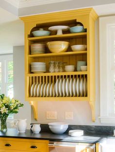 a yellow china cabinet with plates and bowls on it