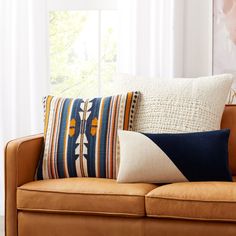 a couch with pillows on top of it in front of a window and a painting