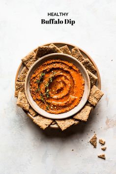 a bowl filled with hummus next to crackers on top of a white table