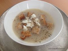 a white bowl filled with soup and croutons on top of a wooden table