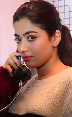 a woman talking on a phone while holding a cellphone up to her ear and looking at the camera