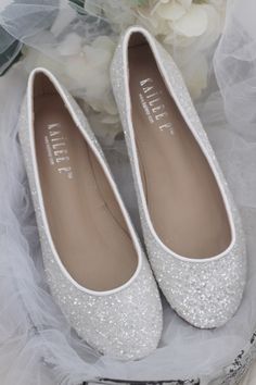 white wedding shoes with silver sequins and tulle on the bottom are sitting next to a bouquet of flowers