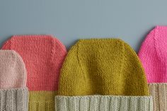 four knitted hats lined up in different colors on a gray background, with one wearing a yellow hat and the other pink