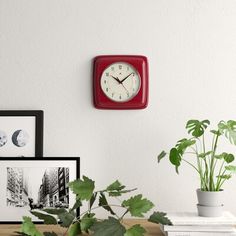 a red square clock mounted to the side of a wall next to a potted plant