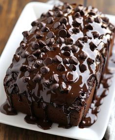 a chocolate cake on a white plate covered in chocolate chips and drizzles