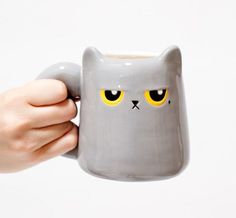 a hand holding a gray mug with yellow eyes