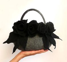 a hand holding a gray and black purse with flowers on the front, while it is being held up by a woman's hand