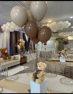 a teddy bear sitting on top of a table with balloons in the shape of animals