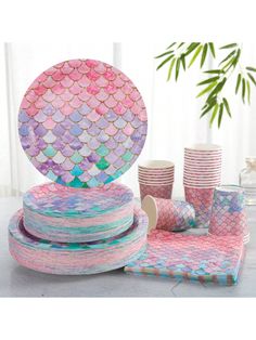 a table topped with plates and cups covered in mermaid fish scale paper napkins next to a potted plant