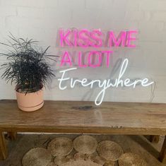 a wooden table topped with lots of potted plants next to a neon sign that says kiss me alot everywhere