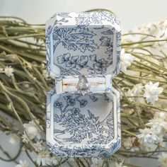 an open ring box sitting on top of a table next to white flowers and greenery