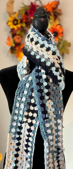 a blue and white crocheted scarf sitting on top of a black mannequin