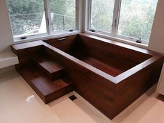 a large wooden bathtub sitting in the middle of a room next to two windows