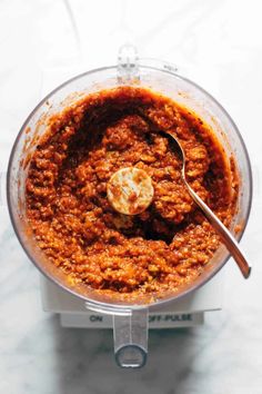 a food processor filled with red sauce on top of a white counter next to a silver spoon