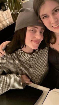 two women sitting next to each other in front of a table with an open book