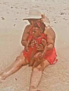 a woman and child sitting on the beach in the sand with their hands around each other