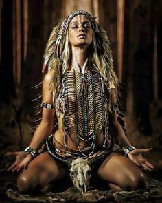 a woman sitting in the middle of a forest with long hair and feathers on her head