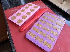 two trays filled with dog treats on top of a red counter next to a pair of scissors