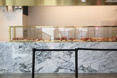 a marble counter top with pastries behind it in a restaurant or bar area that is white and has gold trim around the edges